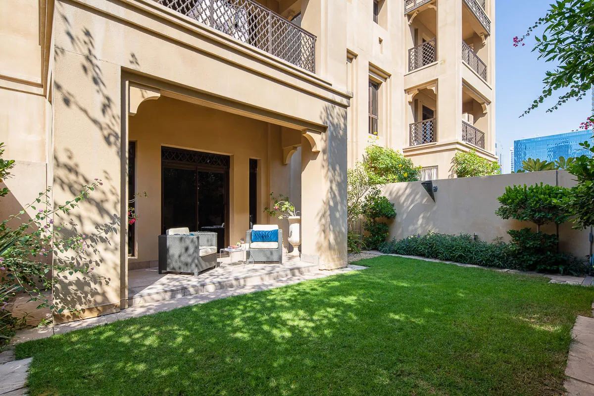 A landscaped courtyard with a lawn, patio seating, and a shaded building entrance.