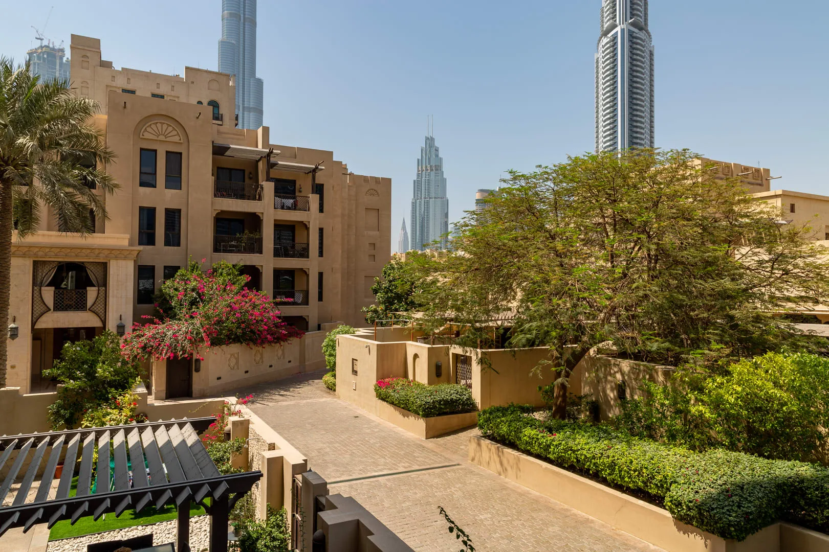 A landscaped courtyard walkway runs between tan buildings and leafy trees.