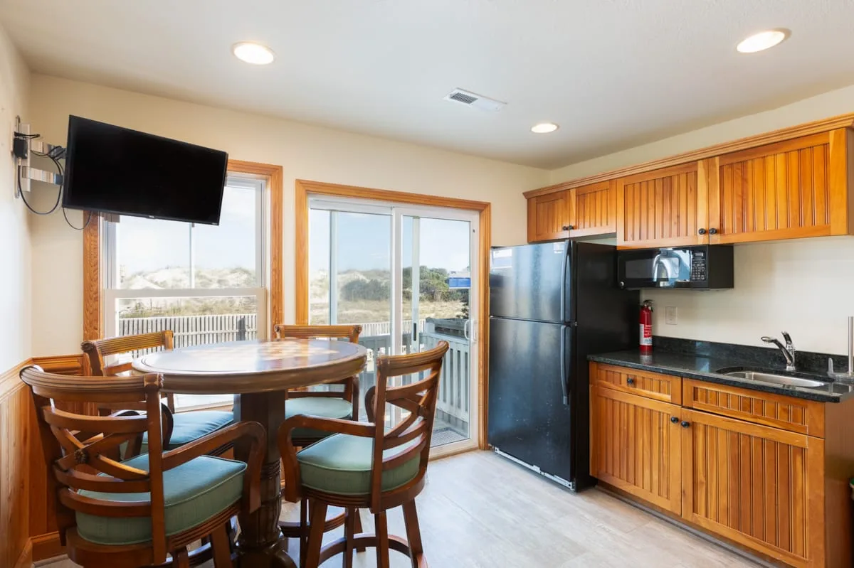 Cocina y comedor con armarios de madera, una mesa y un televisor.