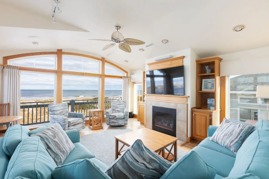 A bright living room opens onto a balcony with a view of the ocean.
