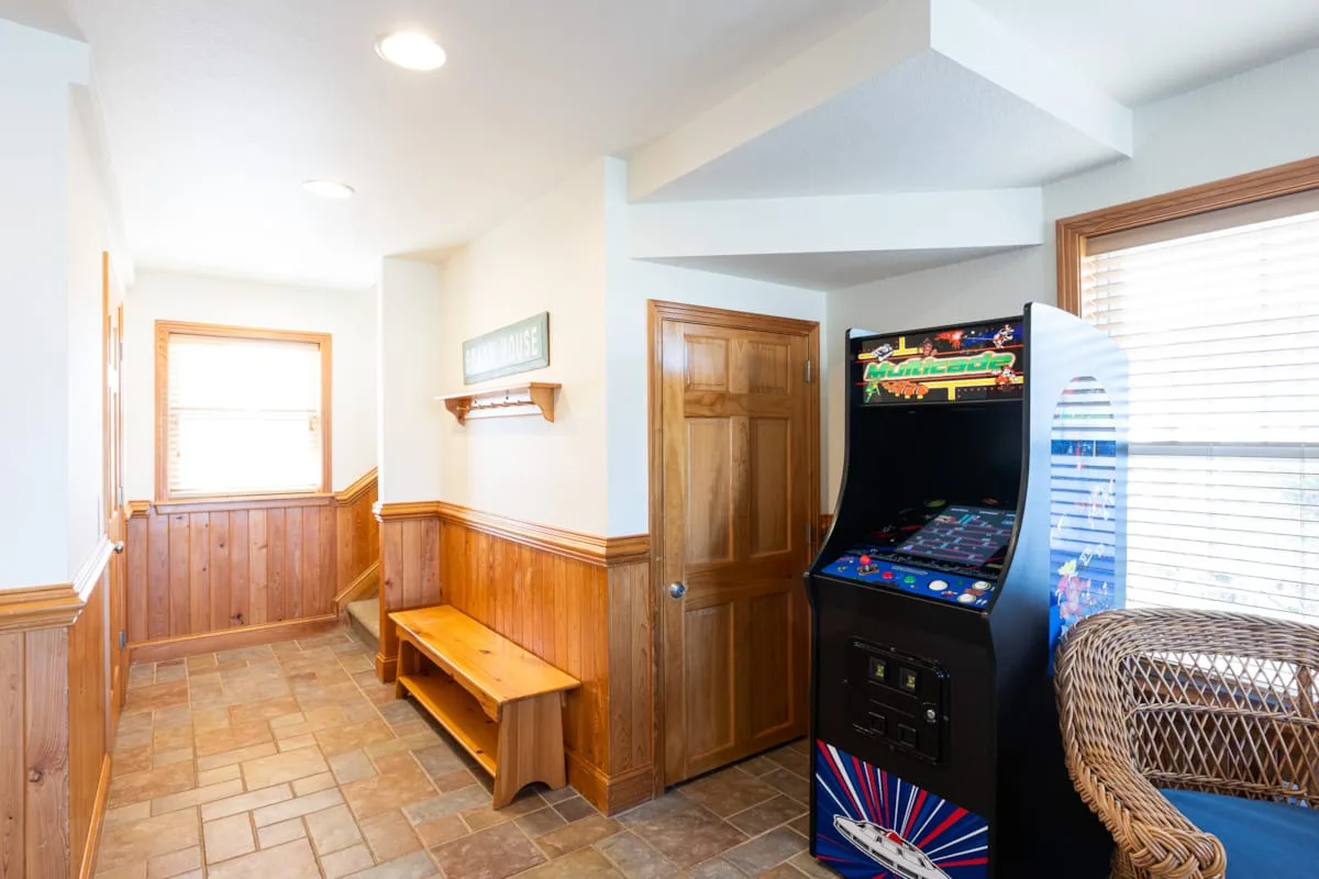 A wood-paneled hallway with a bench and an arcade game beside the windows.