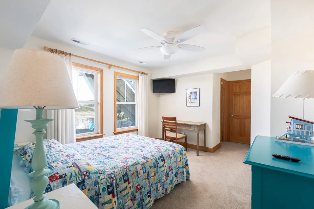 A bedroom with a patterned bedspread, two windows, and a ceiling fan.