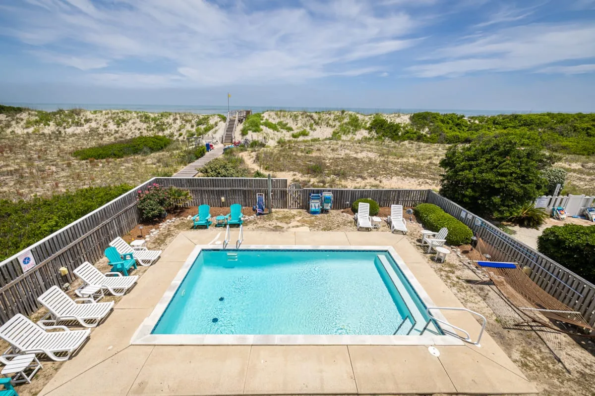 Una piscina exterior cercada está junto a dunas de arena y un sendero hacia la playa.