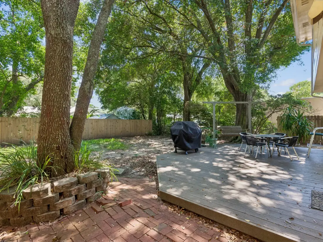 A shaded outdoor deck with a table and seating beneath leafy trees.