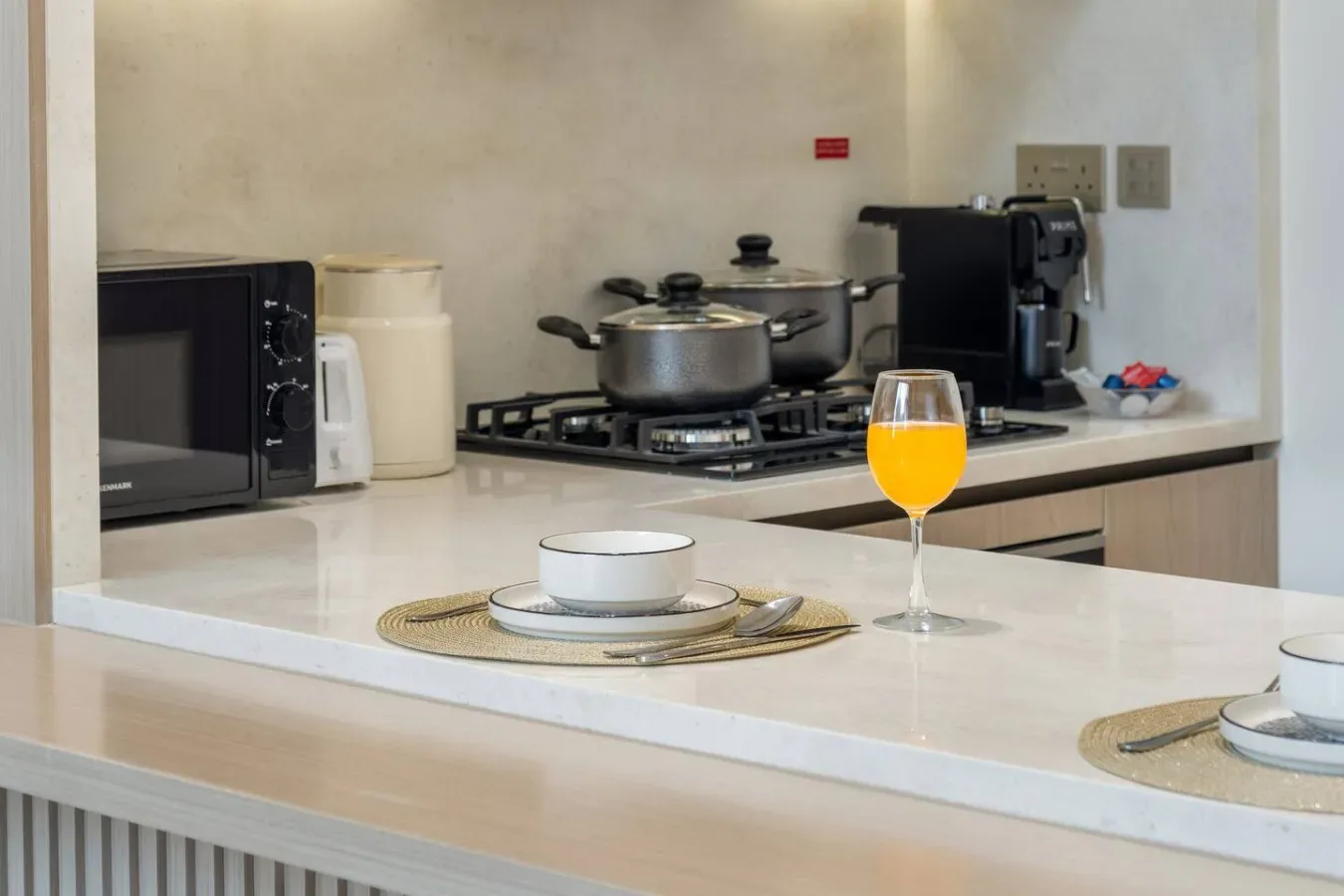 Una encimera de cocina con estufa, utensilios de cocina y un vaso de jugo.
