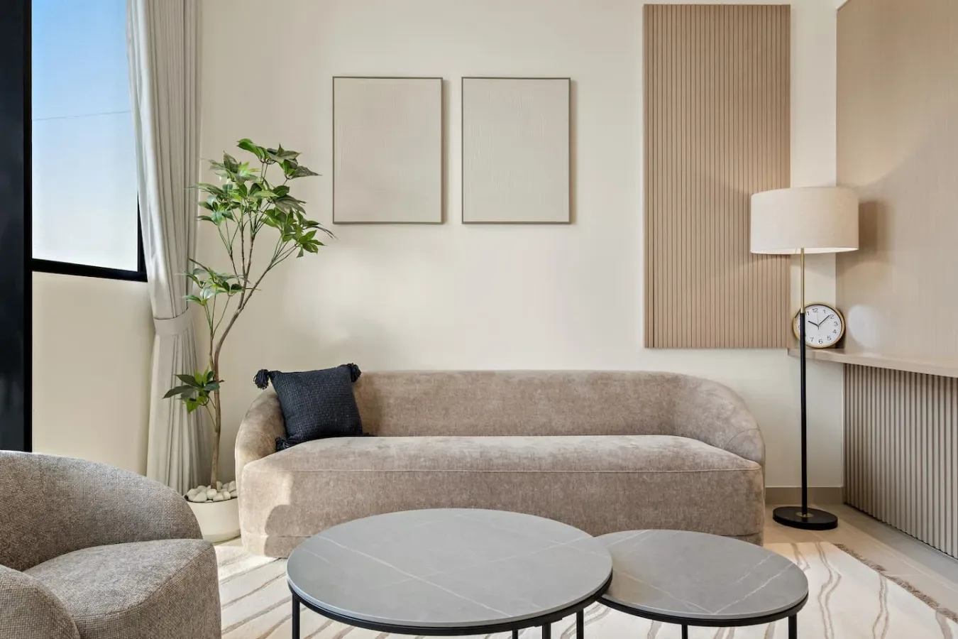 Una sala luminosa con asientos neutros, una lámpara de pie y una planta frondosa.