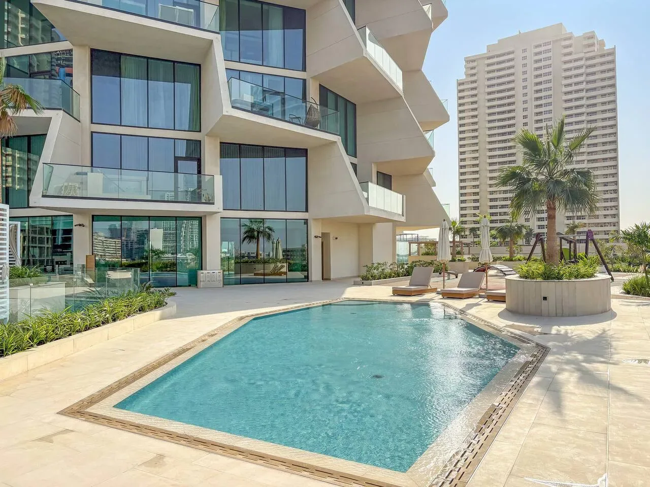 Una piscina al aire libre está junto a un moderno edificio con fachada de vidrio.