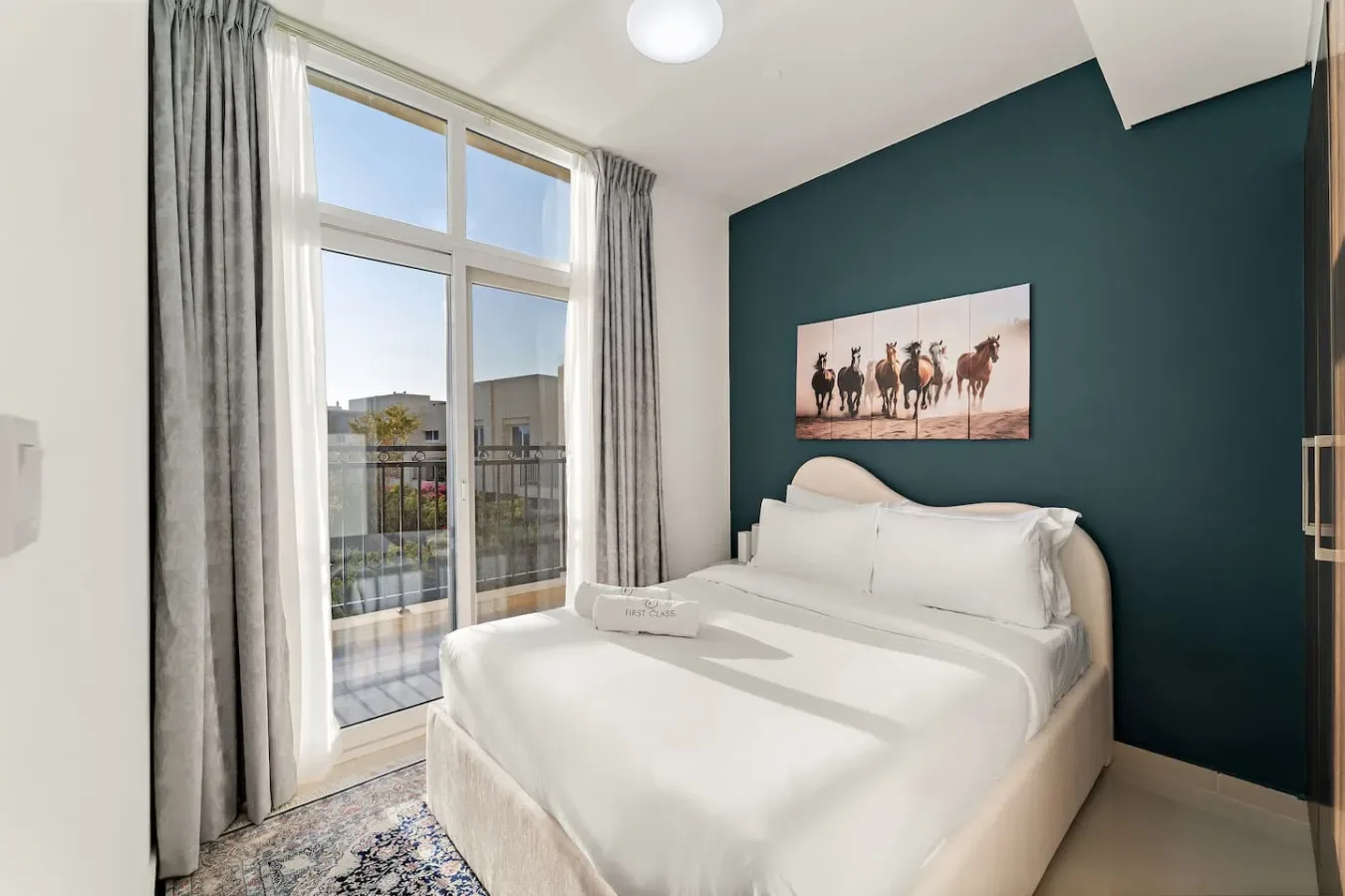 Un dormitorio luminoso con una cama bien hecha junto a ventanas altas.