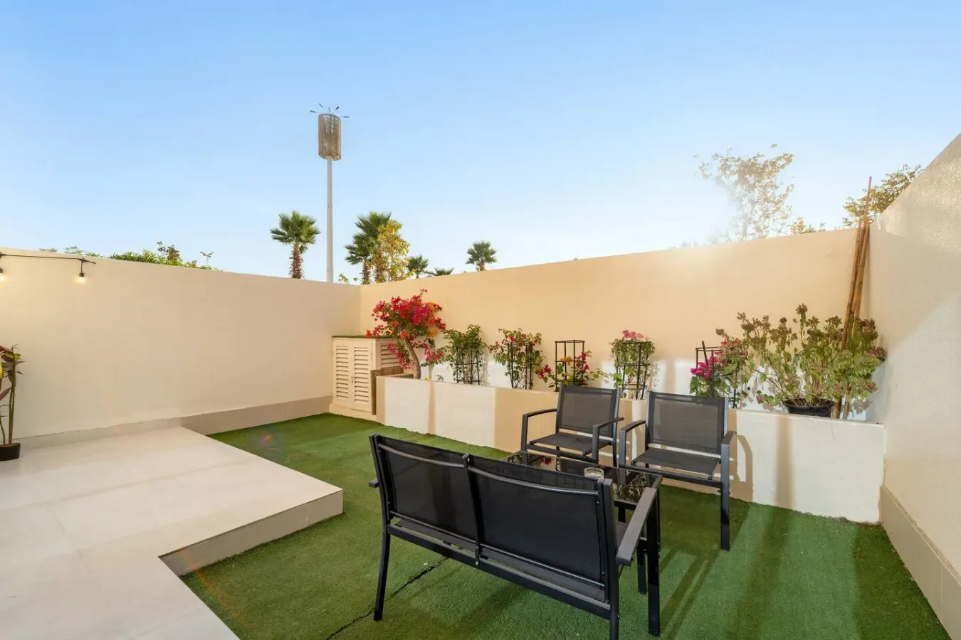 Un patio exterior con asientos, césped artificial y jardineras elevadas.
