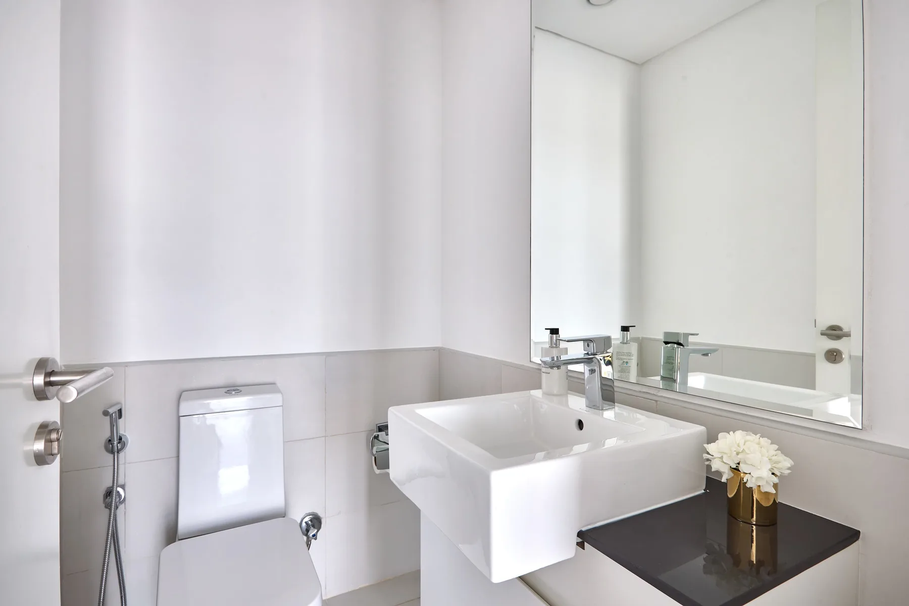 A bright bathroom with a white sink, toilet, and large wall mirror.