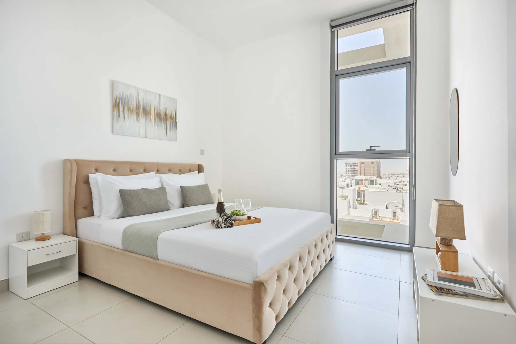 A bright bedroom with a large bed beside a tall window.