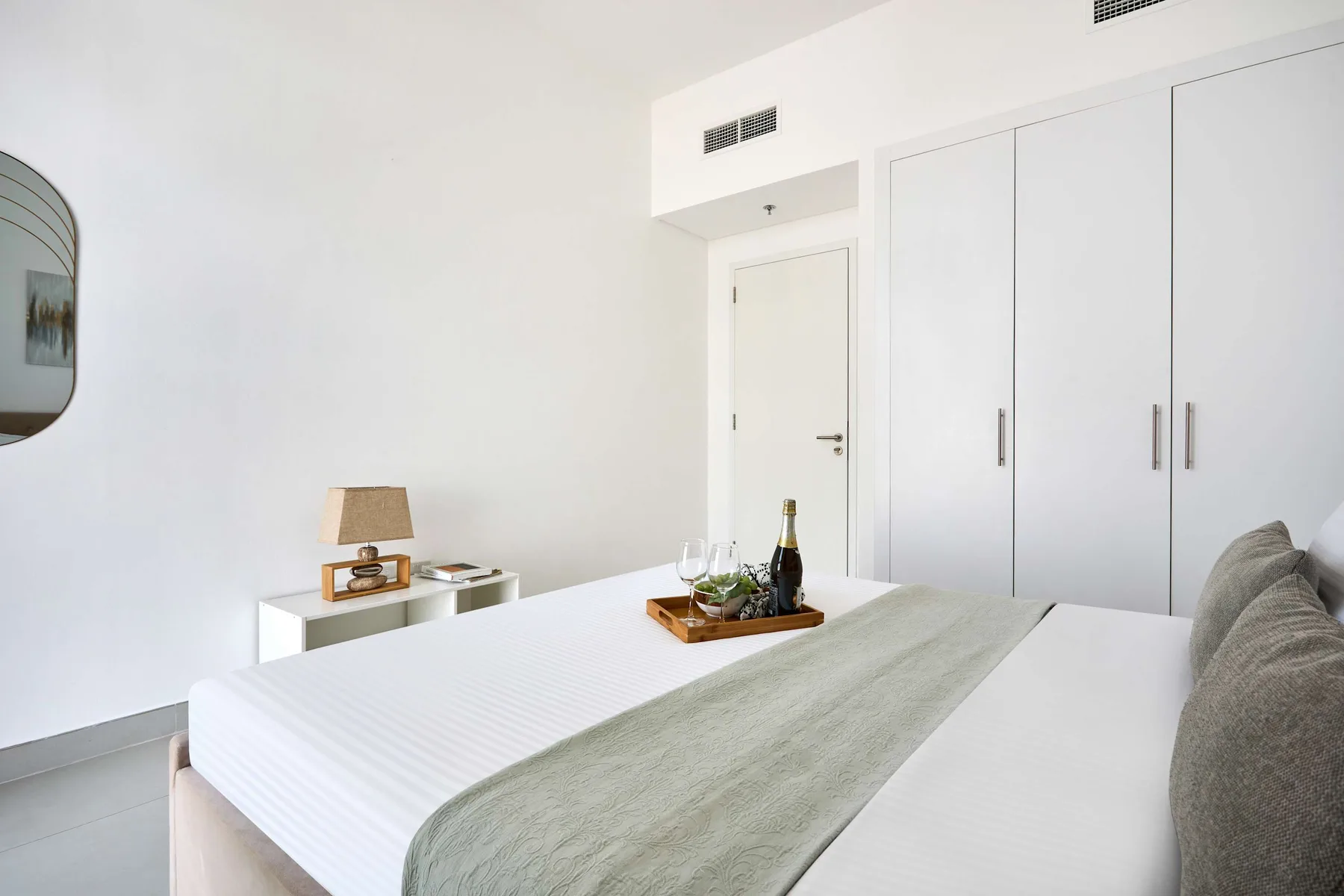 A bright bedroom with a neatly made bed and white built-in wardrobes.