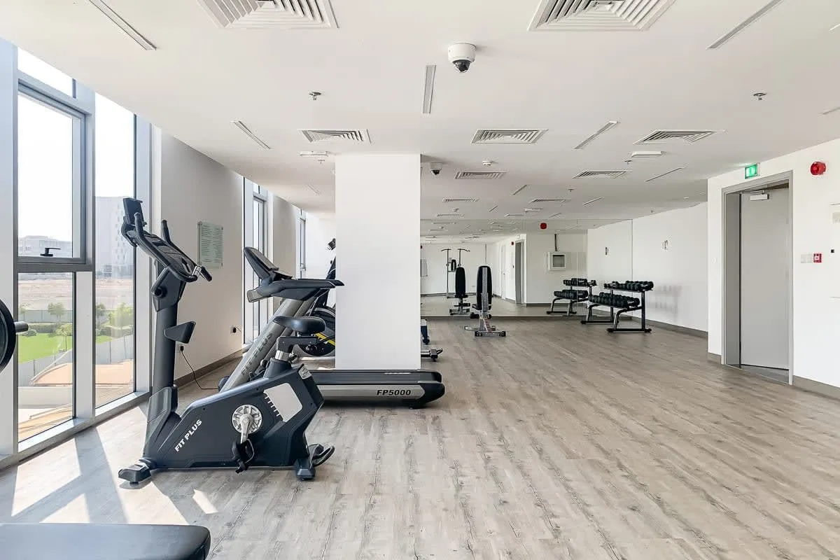 A fitness room with exercise machines beside large windows.
