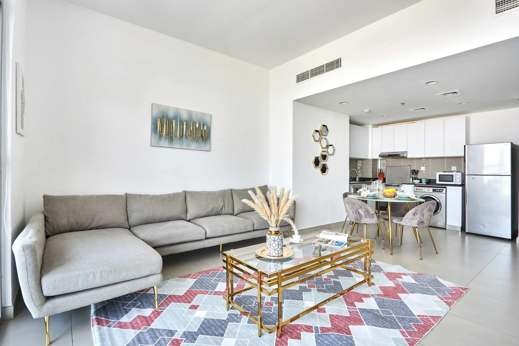 Sala de estar con sofá seccional gris, mesa de centro de vidrio y cocina abierta.
