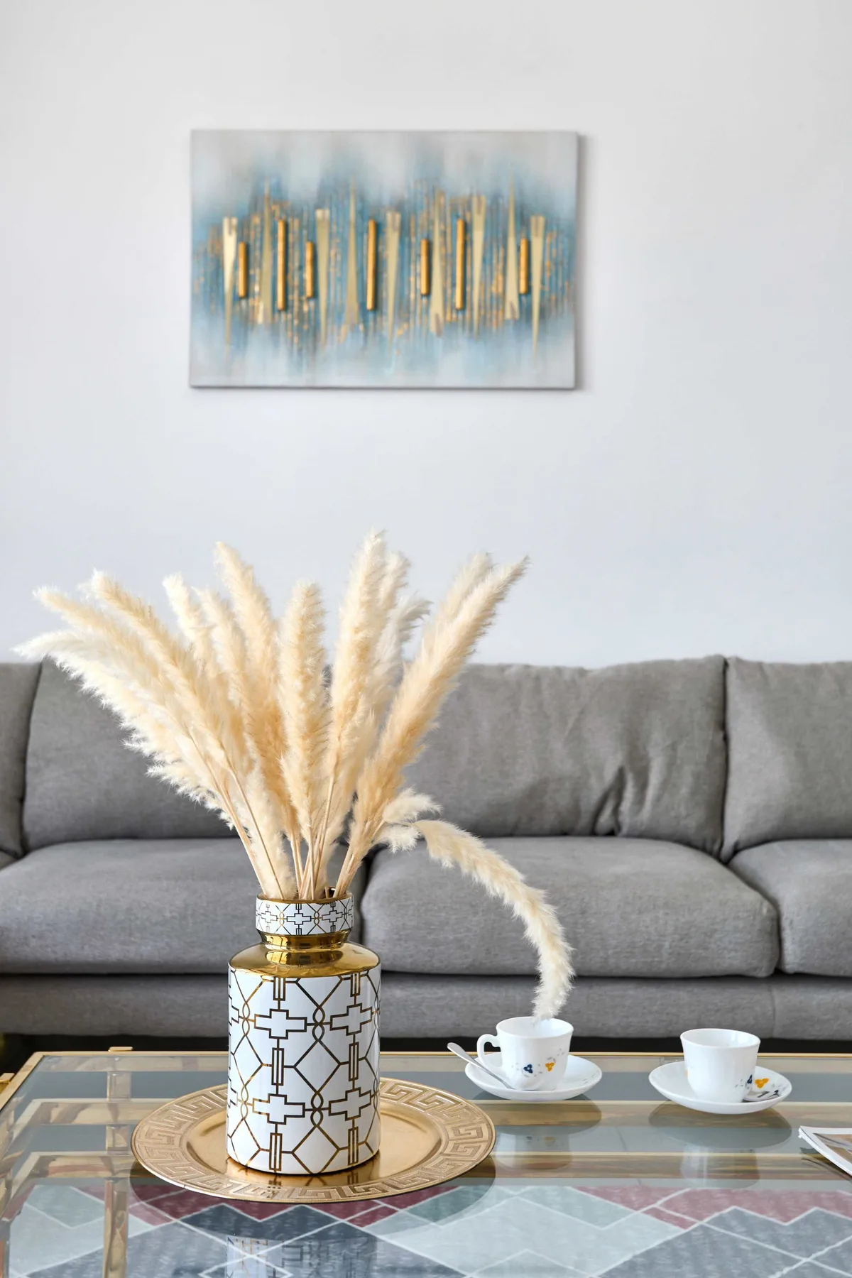 Una sala de estar con un sofá gris, arte decorativo en la pared y una mesa de centro de vidrio.