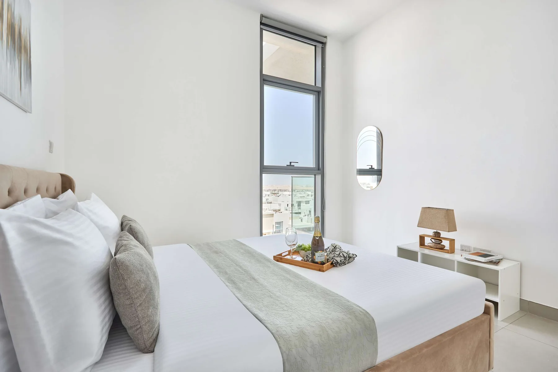 A bright bedroom with a neatly made bed and a tall window.