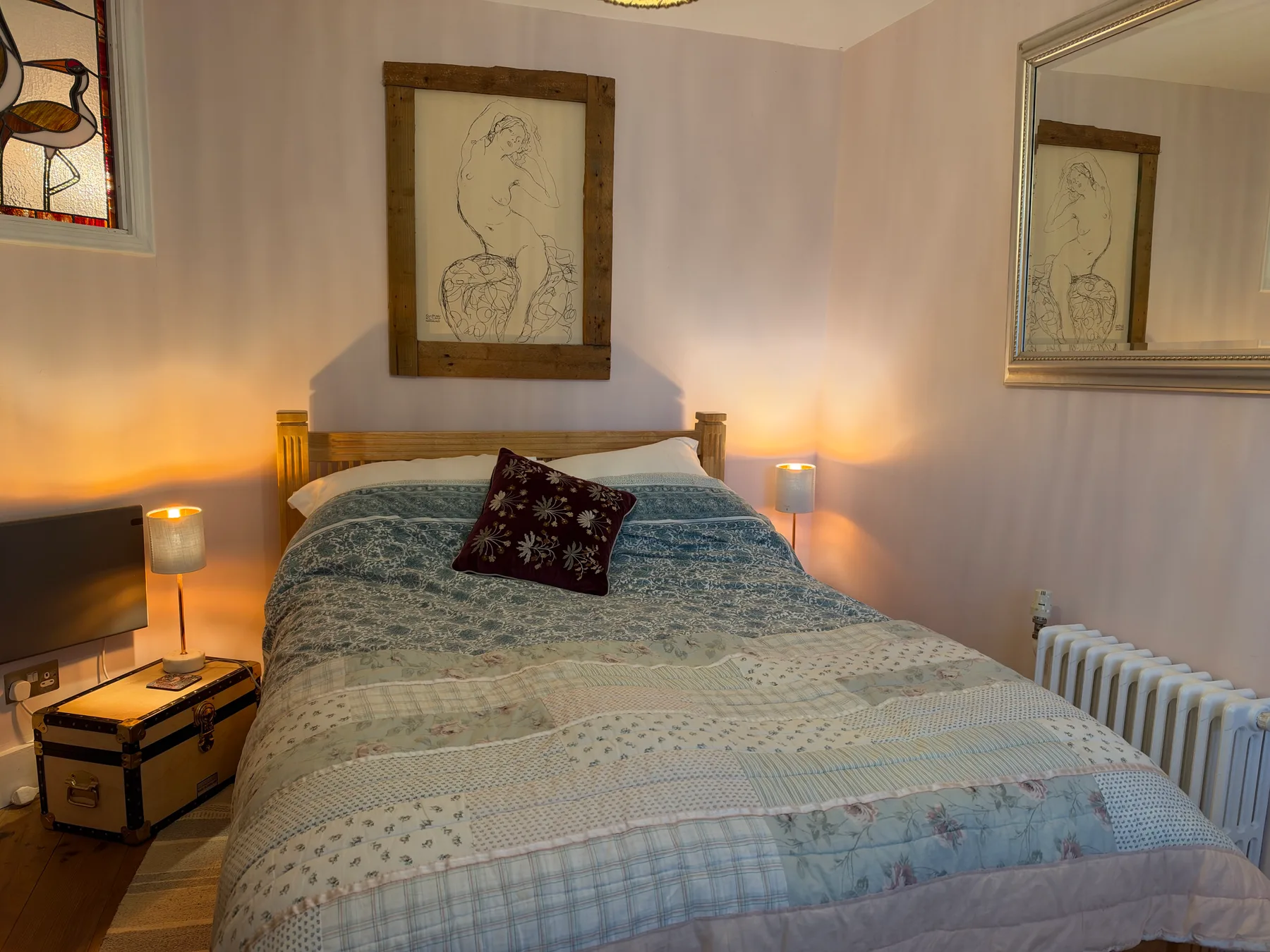 A bedroom with a made bed, bedside lamps, and framed artwork.