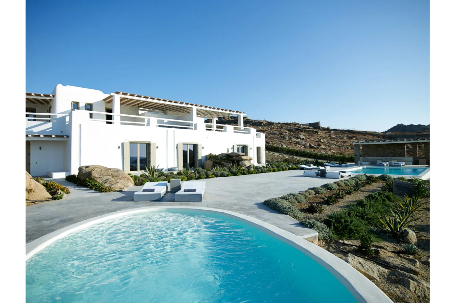 A modern white villa beside a curved swimming pool and landscaped grounds.