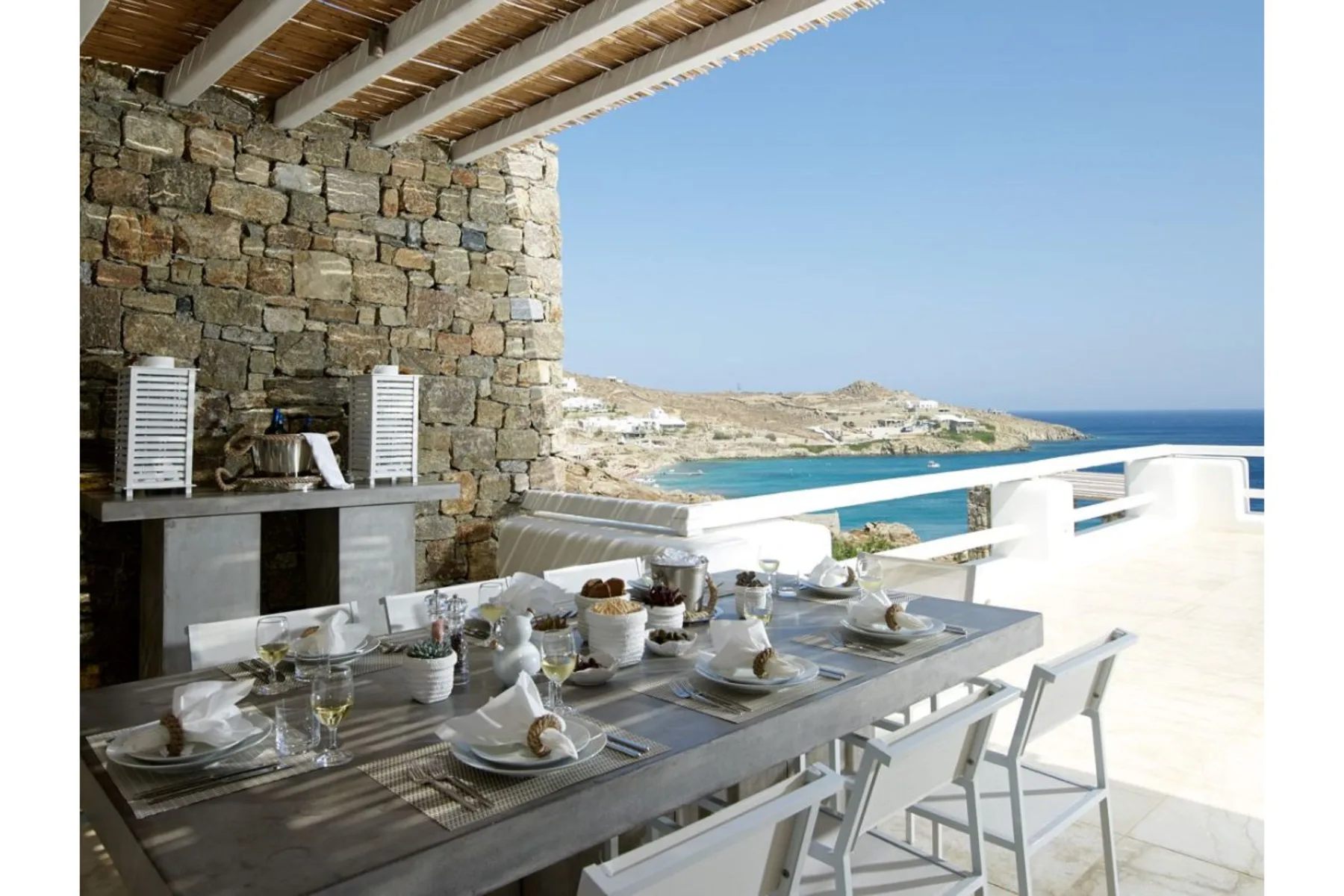An outdoor dining area overlooks the sea beside a stone wall.