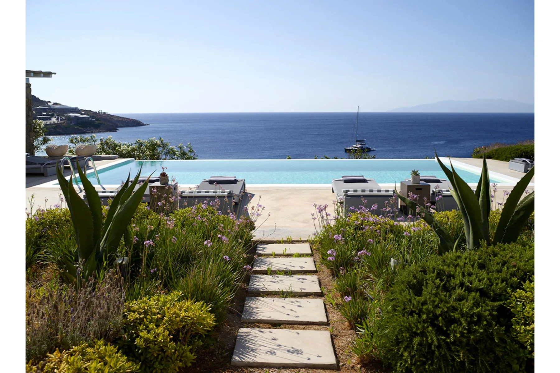 A landscaped garden path leads to a pool overlooking the sea.