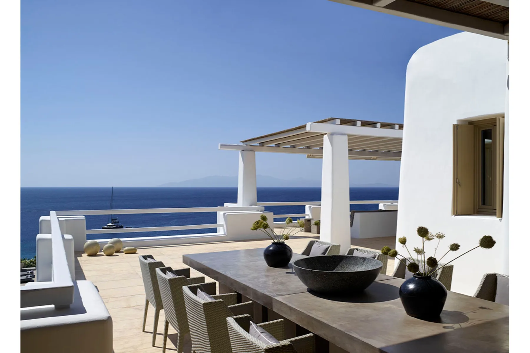 A seaside terrace with a long dining table overlooking the water.