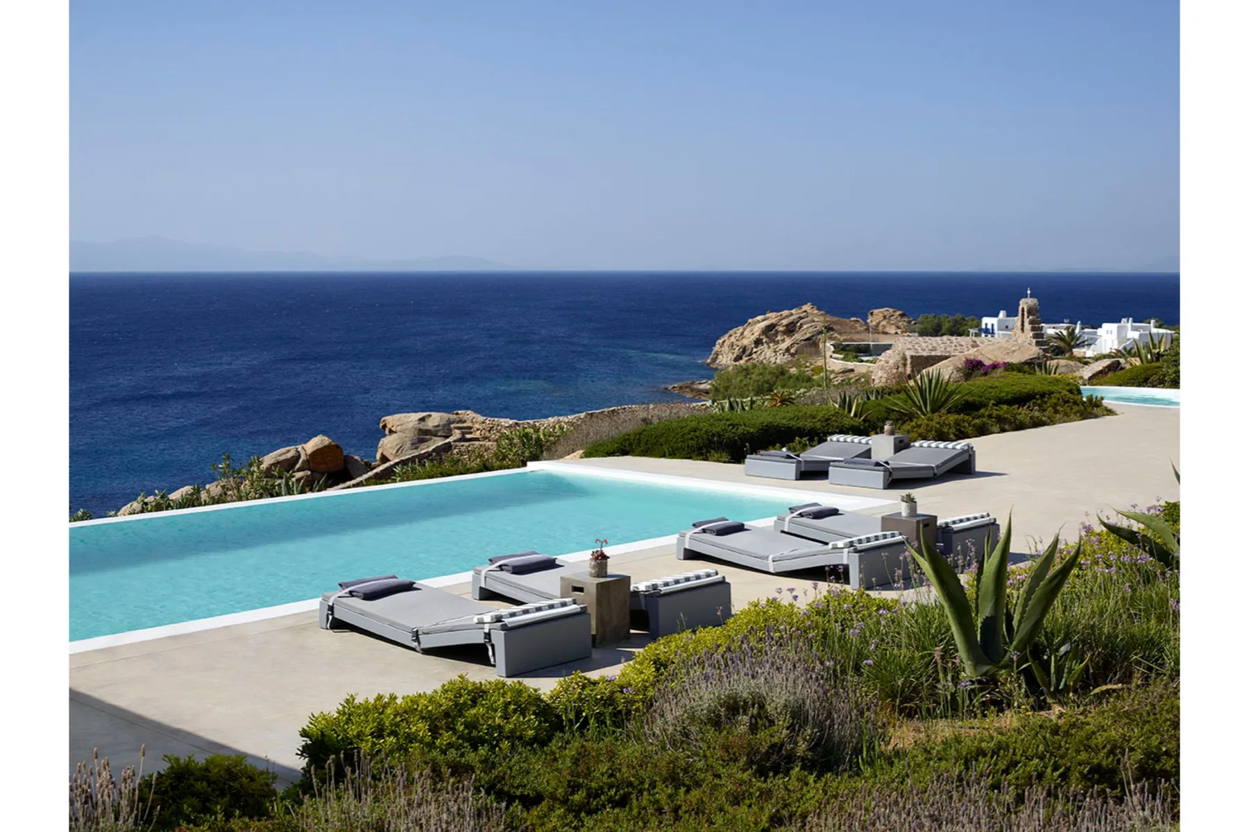 An outdoor poolside terrace overlooks the sea, with loungers beside the water.