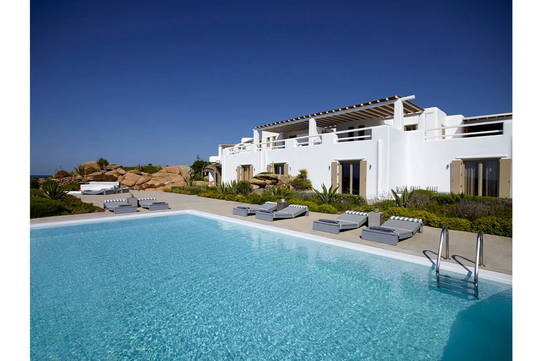 A swimming pool beside a white building, with lounge seating along the edge.