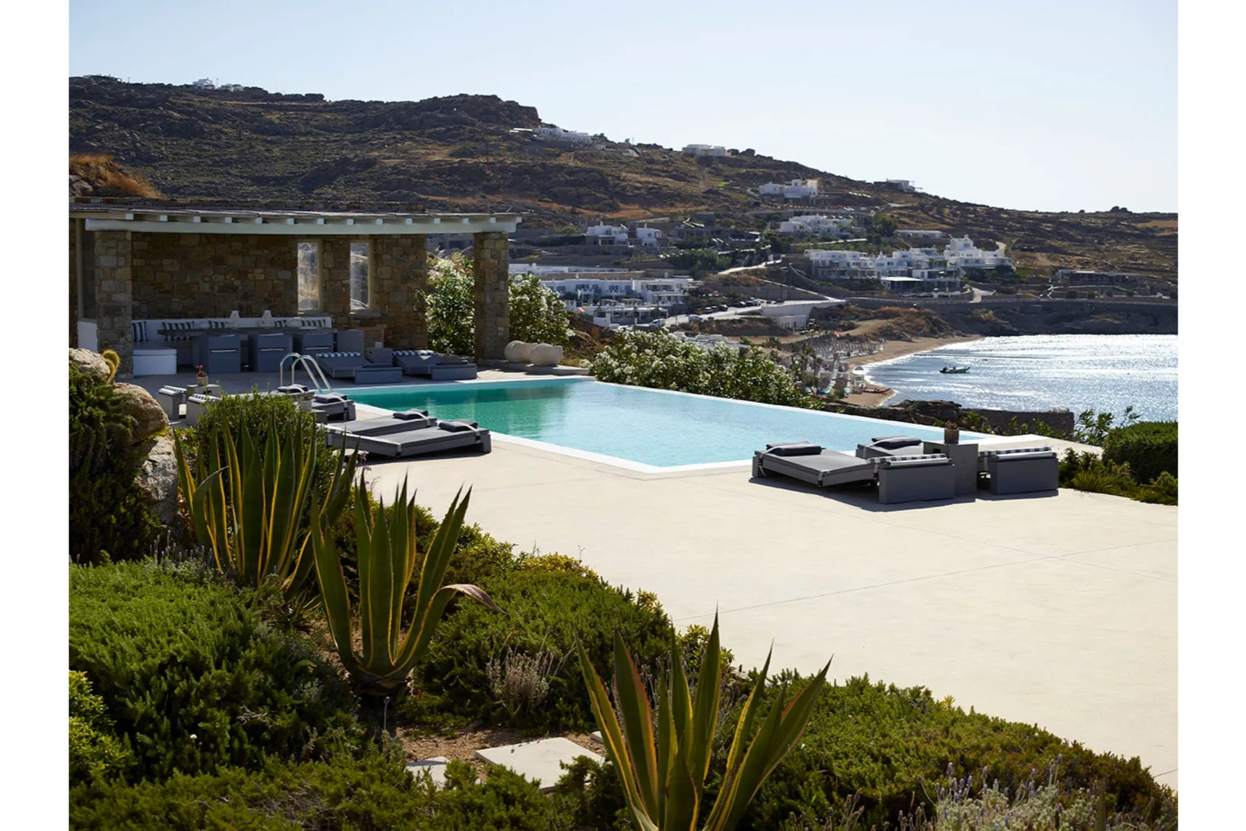 An outdoor pool and sun loungers overlook a coastal hillside.