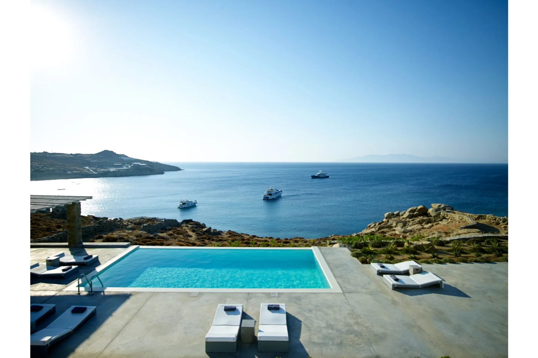 A swimming pool overlooks the sea, with boats visible offshore.