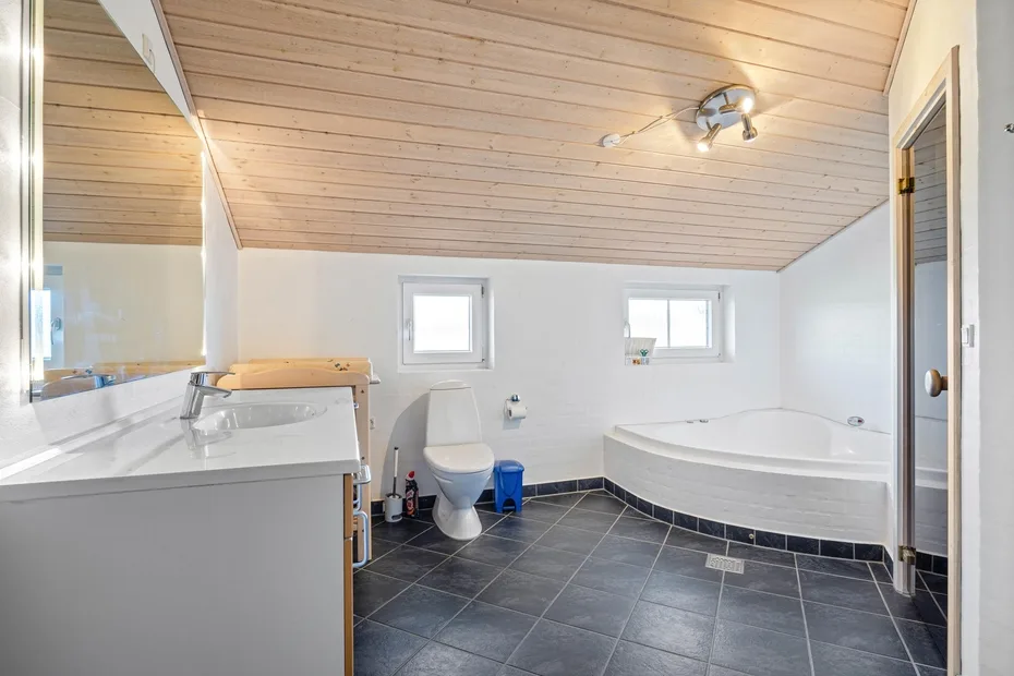 Un baño luminoso con bañera, inodoro y suelo de baldosas.