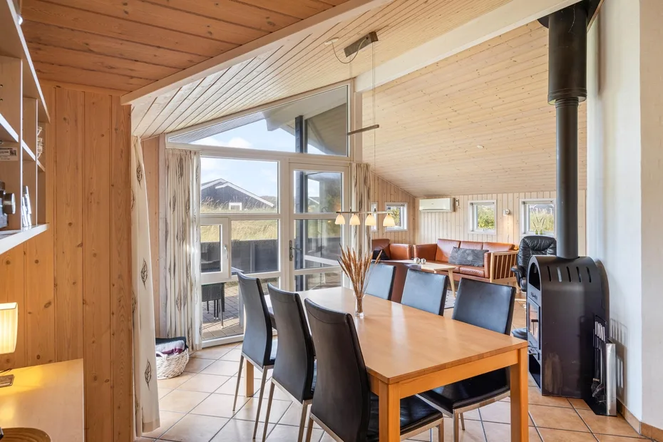 Una mesa de comedor de madera y asientos están bajo un techo inclinado de madera en una habitación luminosa.