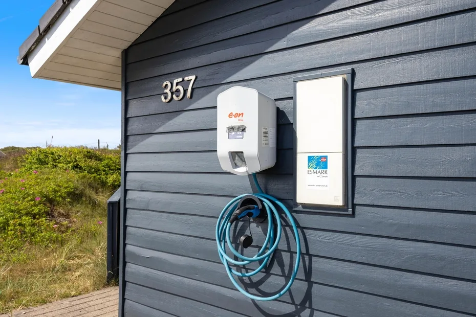 Un cargador para vehículos eléctricos está instalado en la pared exterior oscura de un edificio.