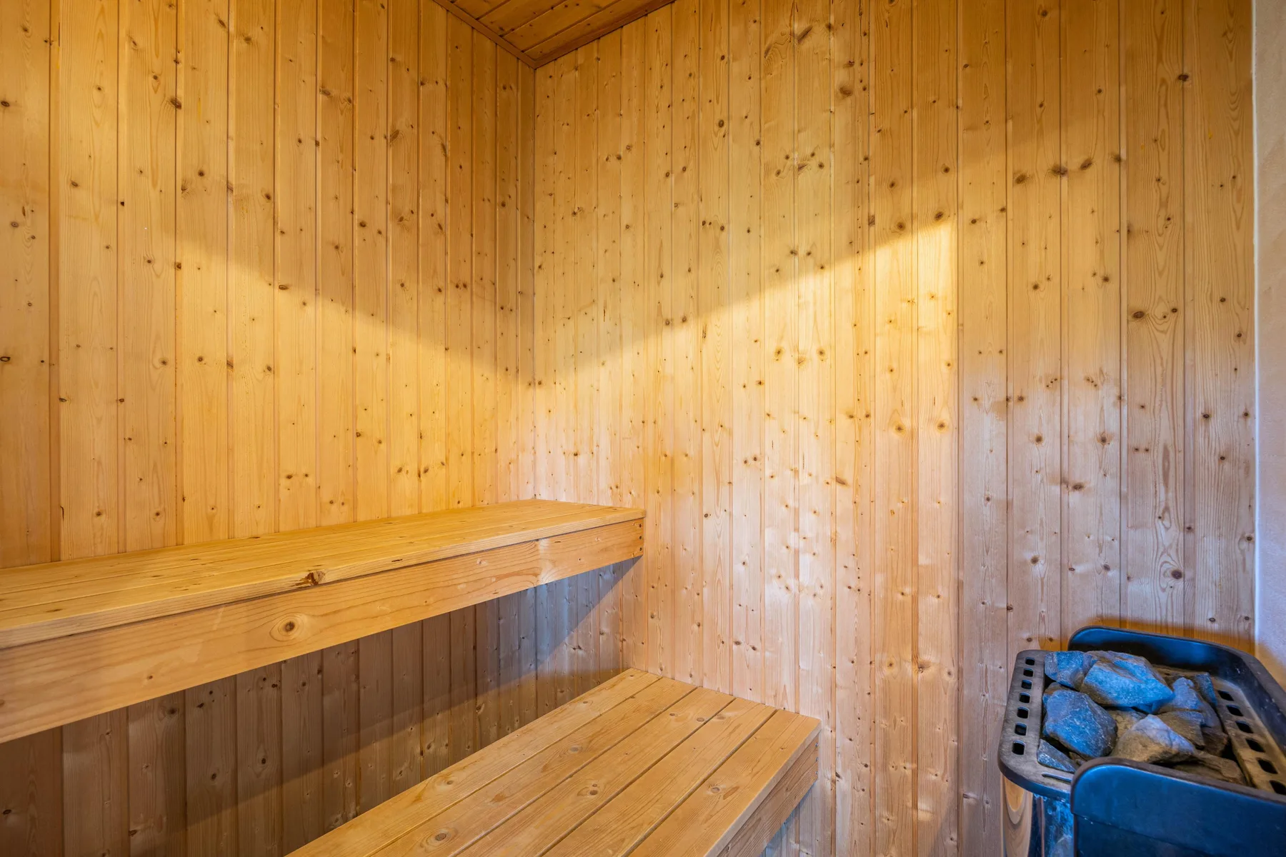 Sauna revestida de madera con bancos escalonados y un calentador con piedras.
