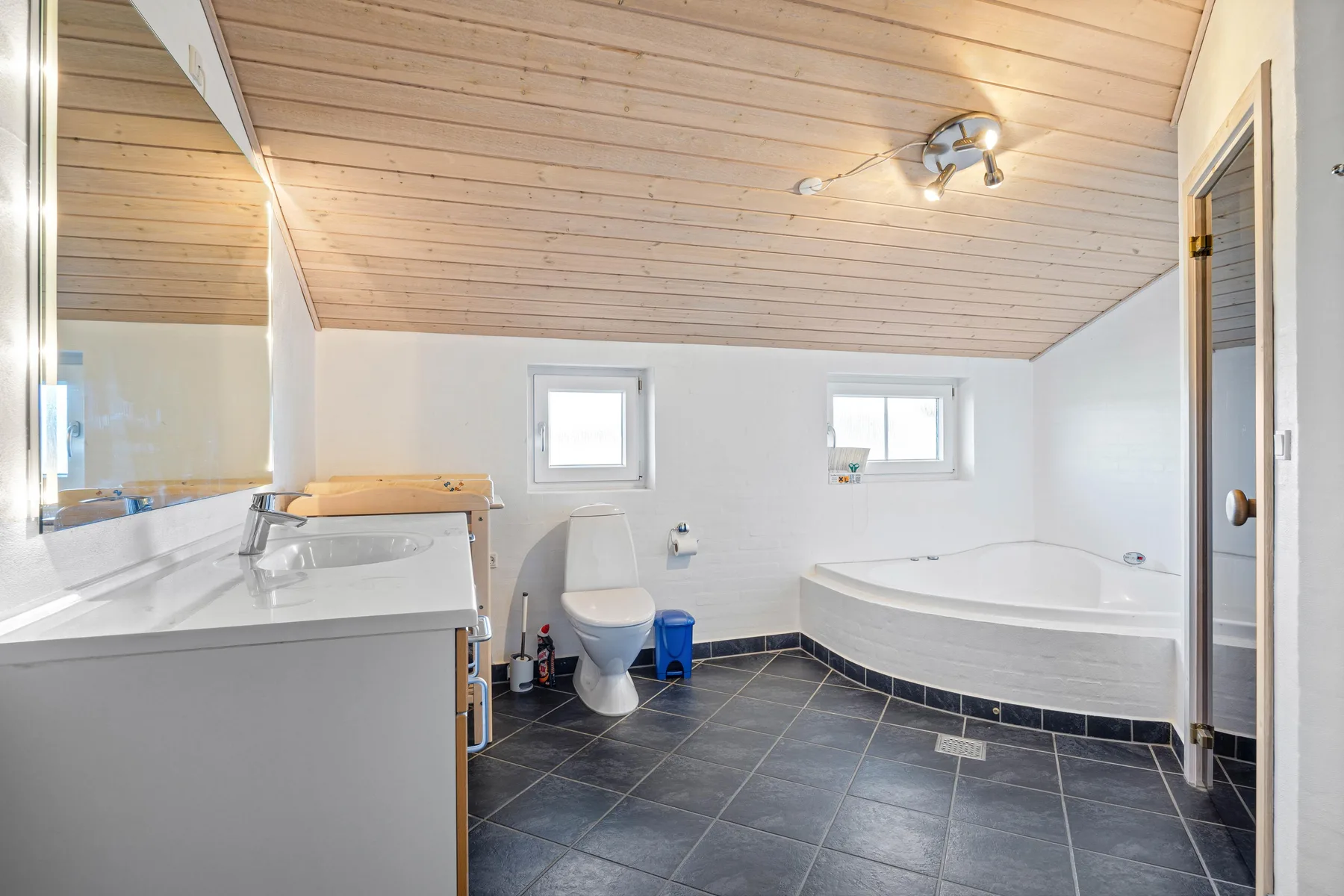 Un baño con bañera, inodoro y lavabo bajo un techo inclinado revestido de madera.