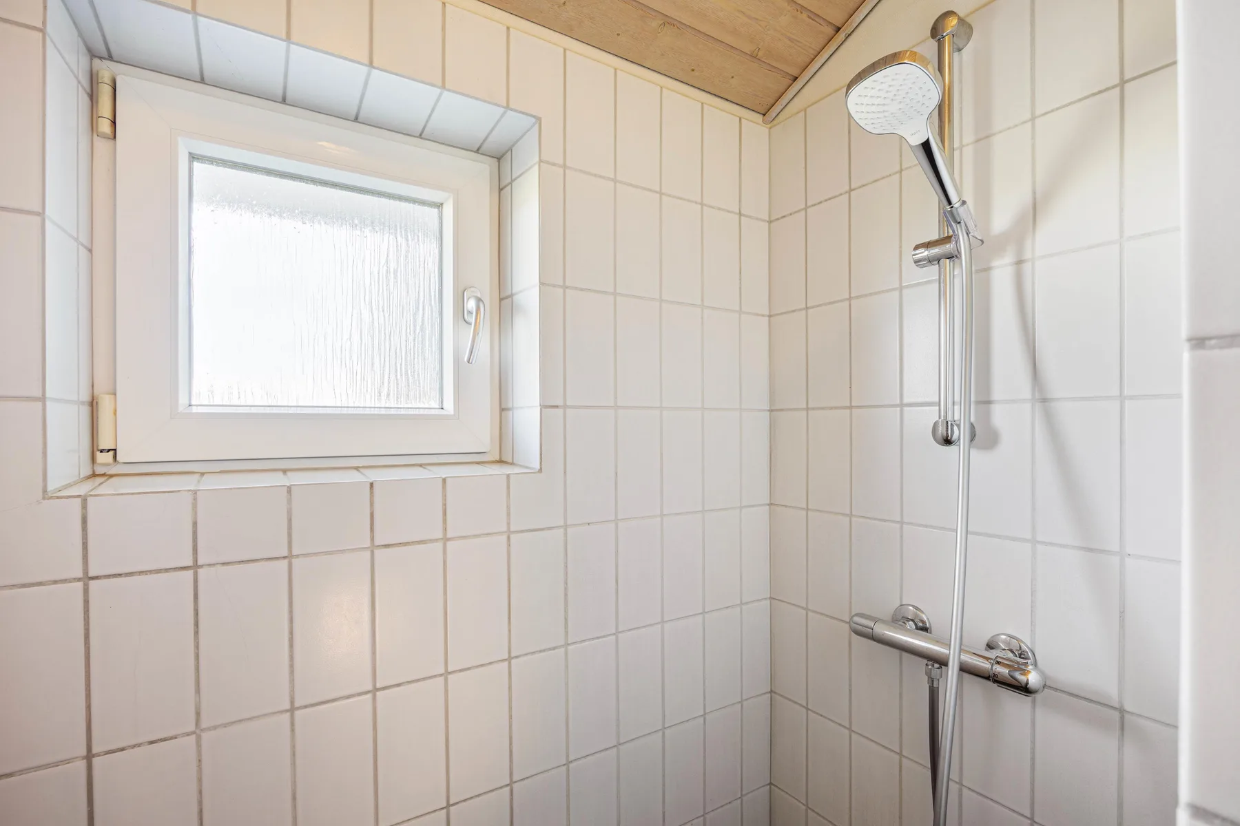 Una ducha en un baño alicatado está junto a una pequeña ventana translúcida.