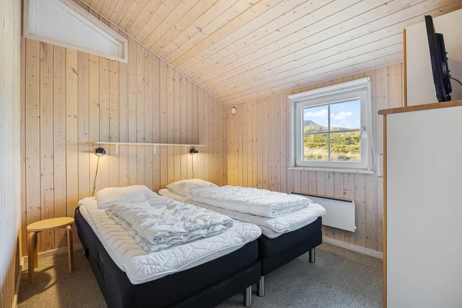 Dormitorio con dos camas bajo un techo inclinado revestido de madera.