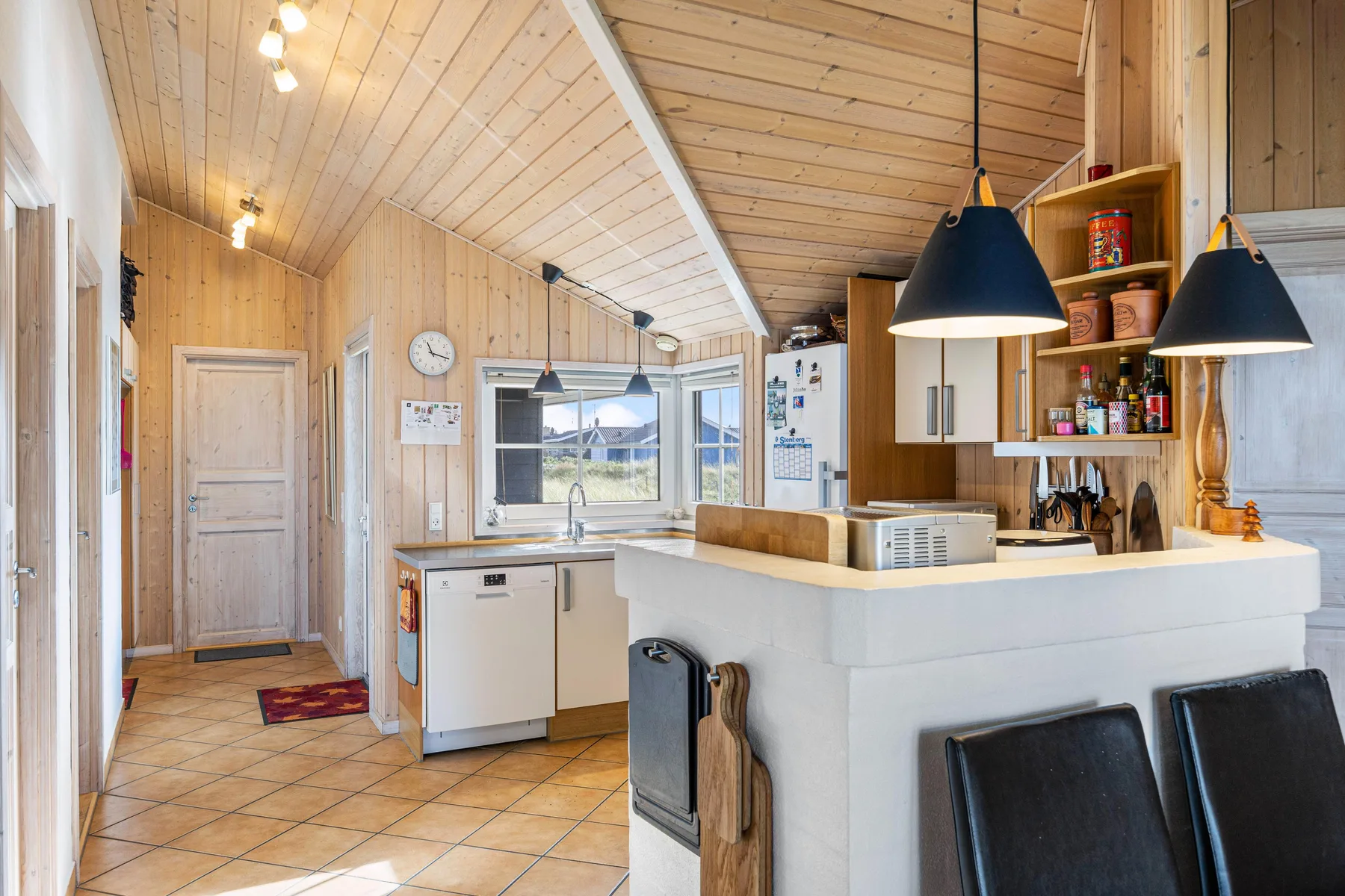Una cocina luminosa revestida de madera, con encimera, fregadero y asientos.