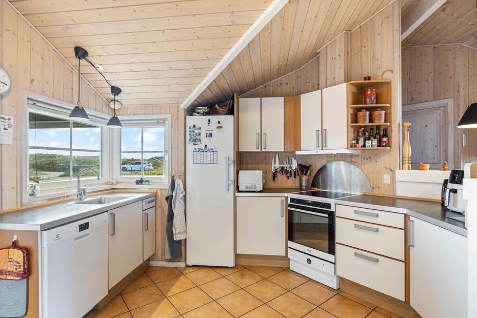 Una cocina luminosa con paredes de madera, armarios blancos y ventanas grandes.