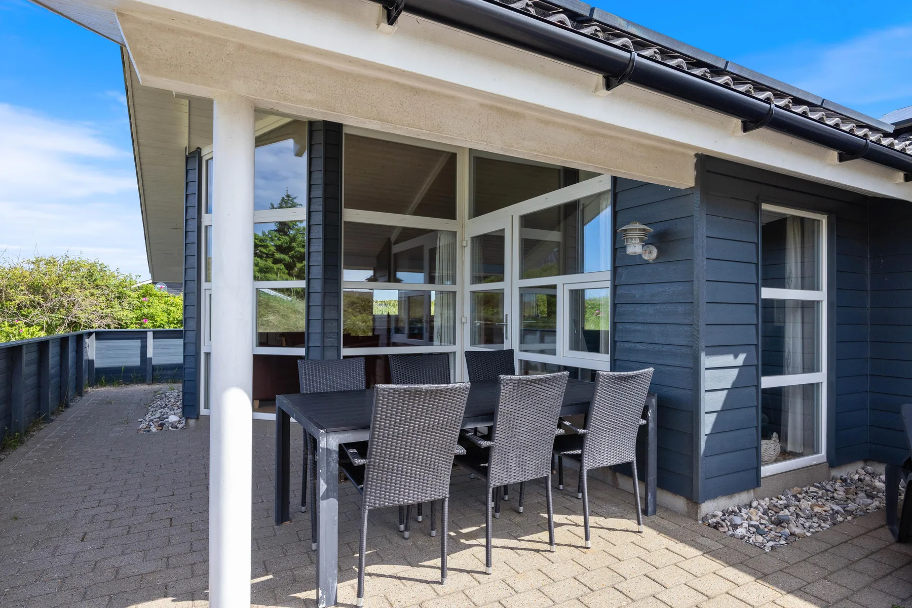 Comedor exterior cubierto junto a una casa, con una mesa y asientos.