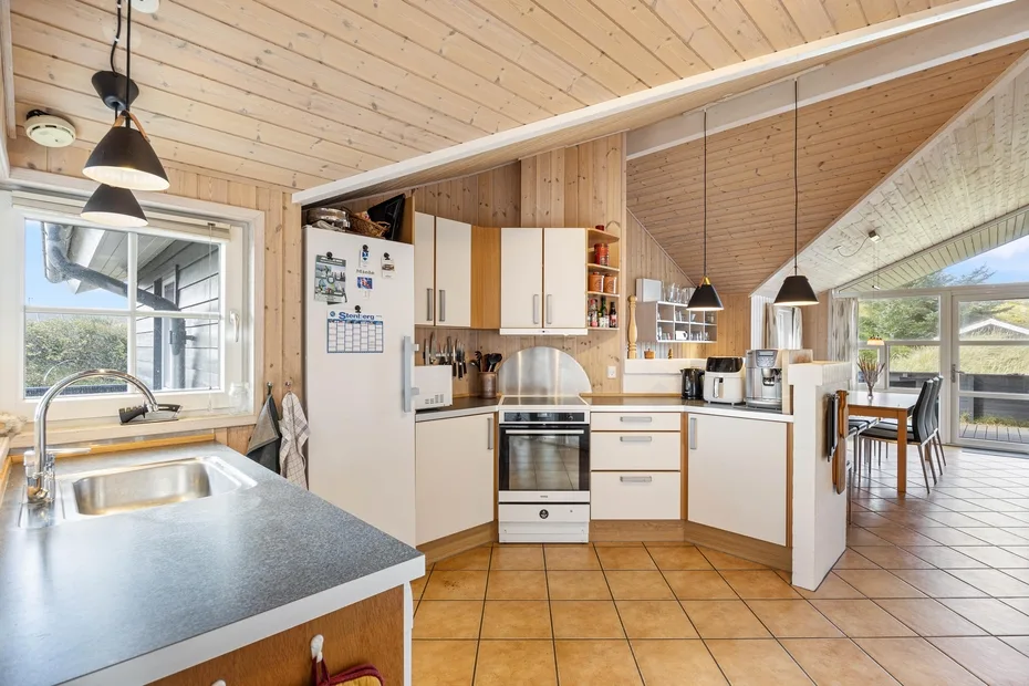 Una cocina luminosa con encimeras, armarios y una mesa de comedor junto a las ventanas.