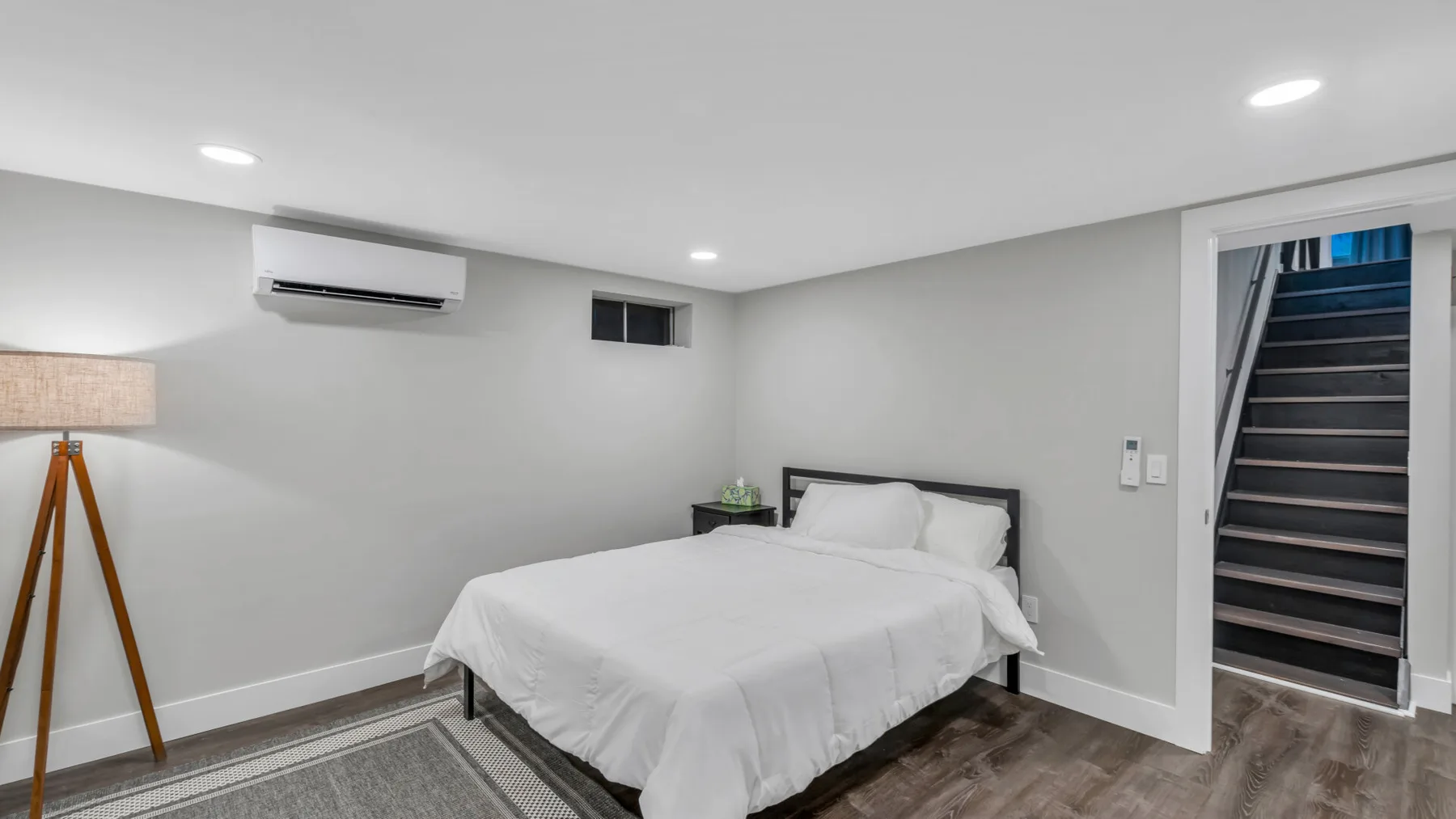 A bedroom with a bed and a staircase visible through the open doorway.