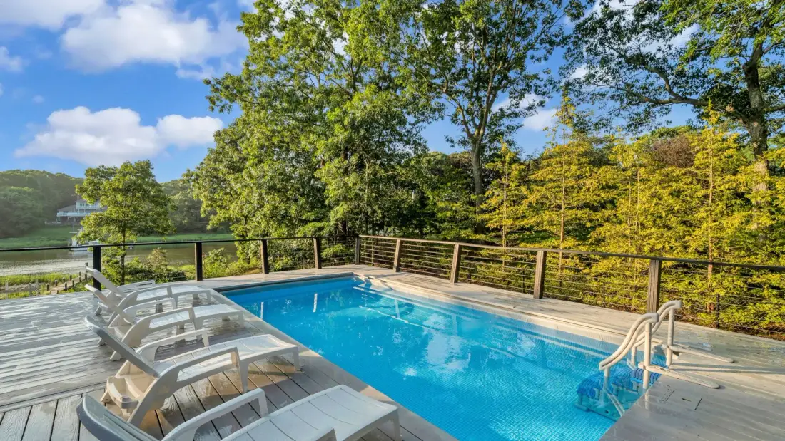 An outdoor swimming pool sits on a wooden deck surrounded by trees.