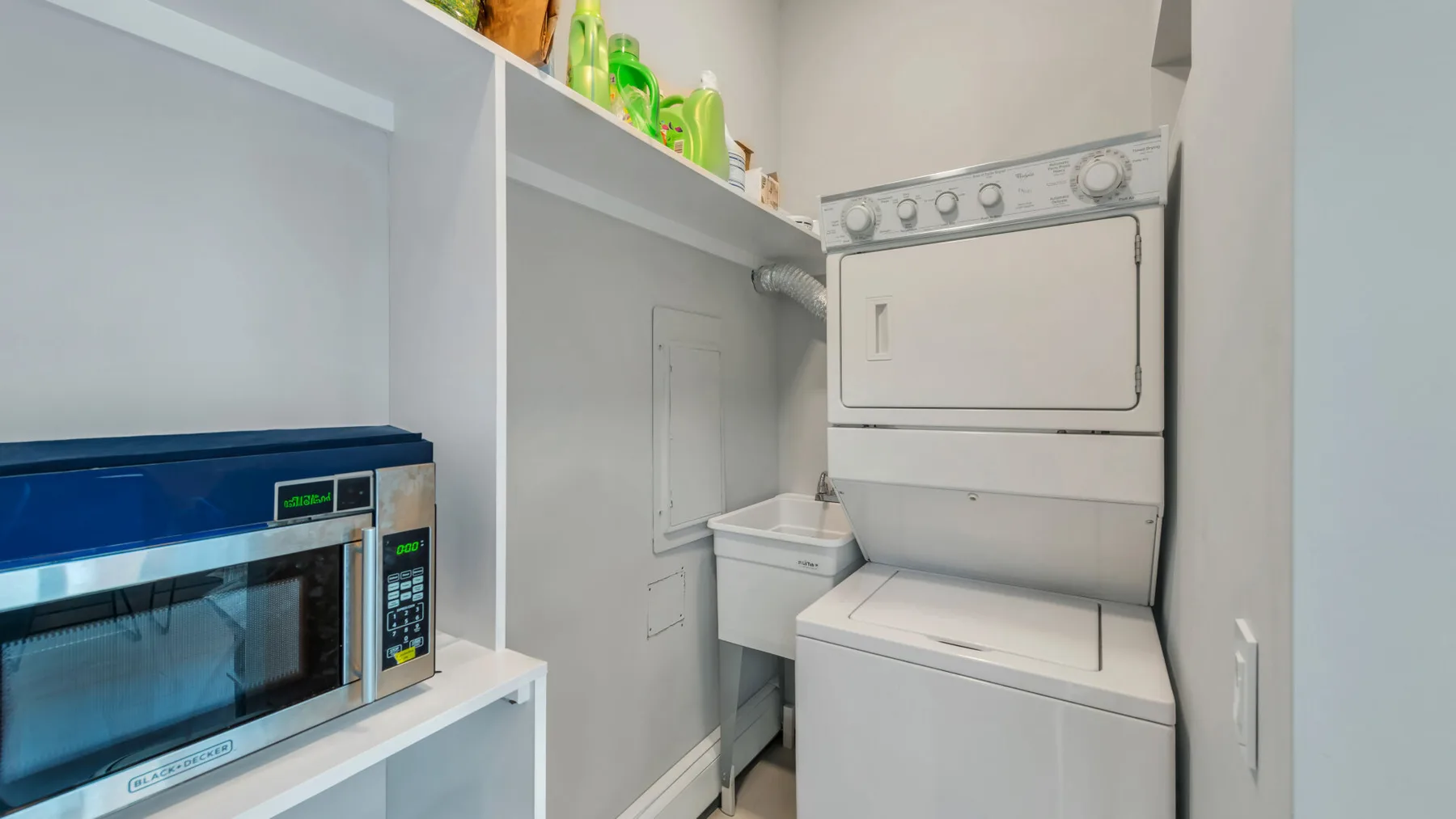 A compact laundry area with stacked laundry machines and a microwave on a shelf.
