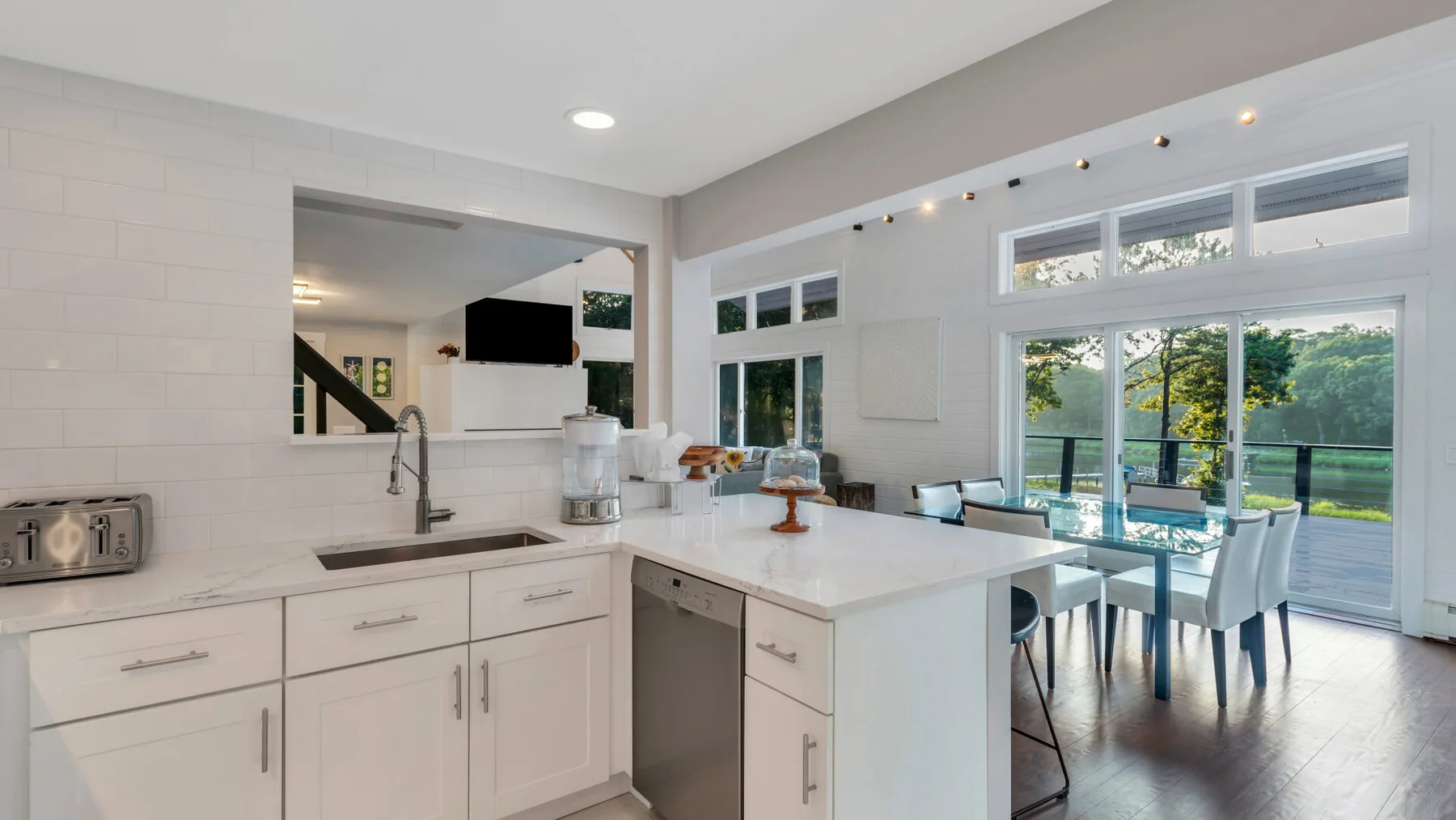 A bright open-plan kitchen and dining area with large windows overlooking greenery.