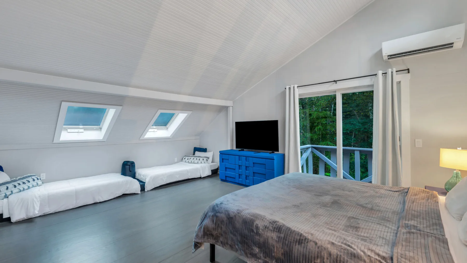 A bright bedroom with beds, a large bed, and glass doors overlooking greenery.