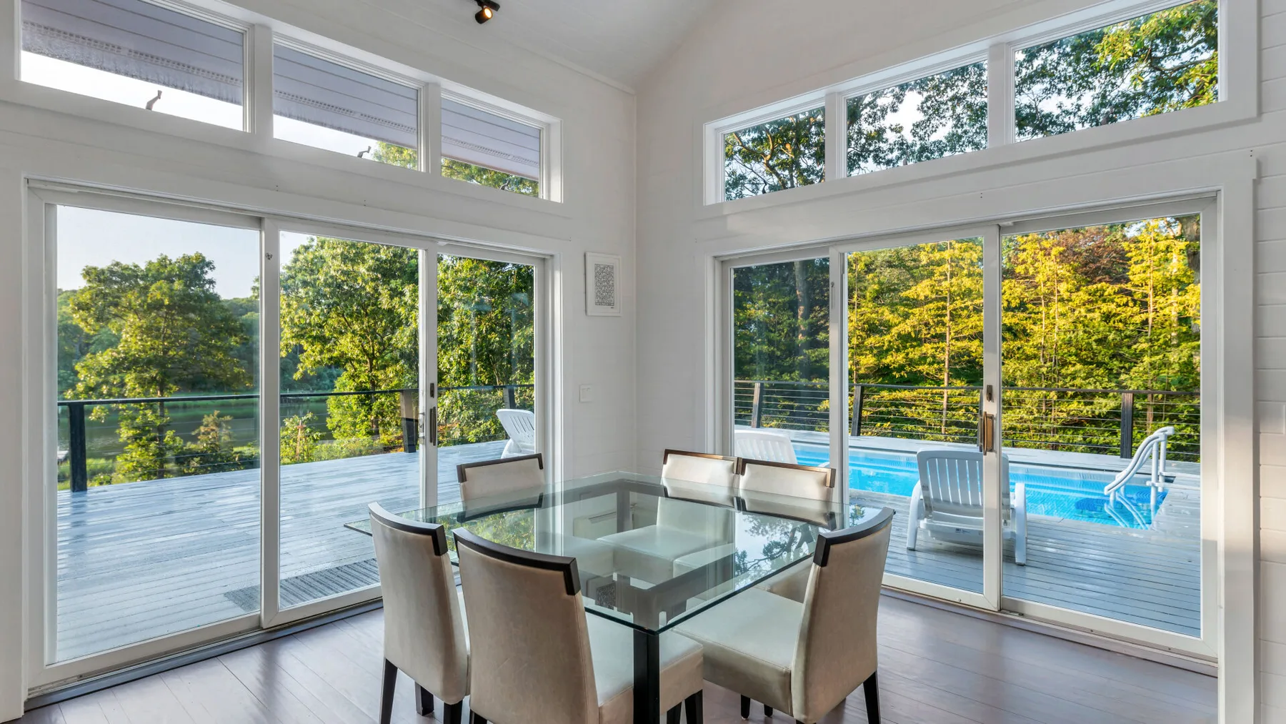 A bright dining area with glass doors opening onto a deck beside a swimming pool.