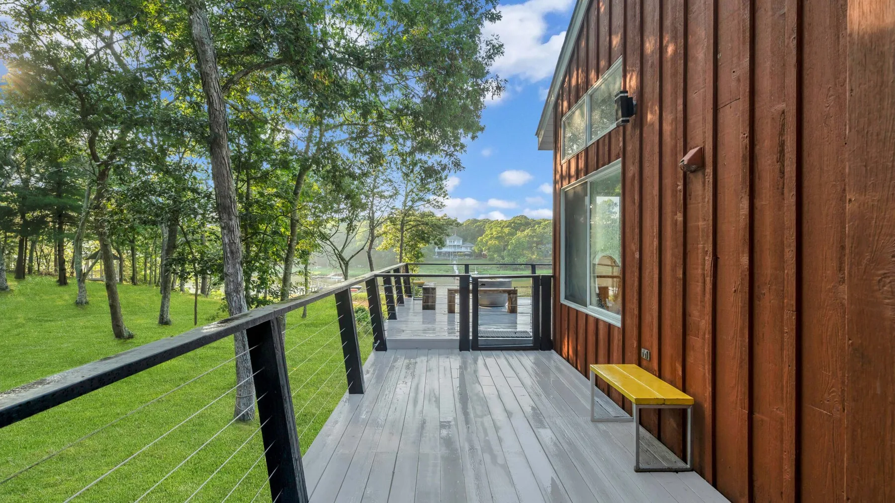 A wooden deck runs alongside a building, overlooking a green lawn and trees.