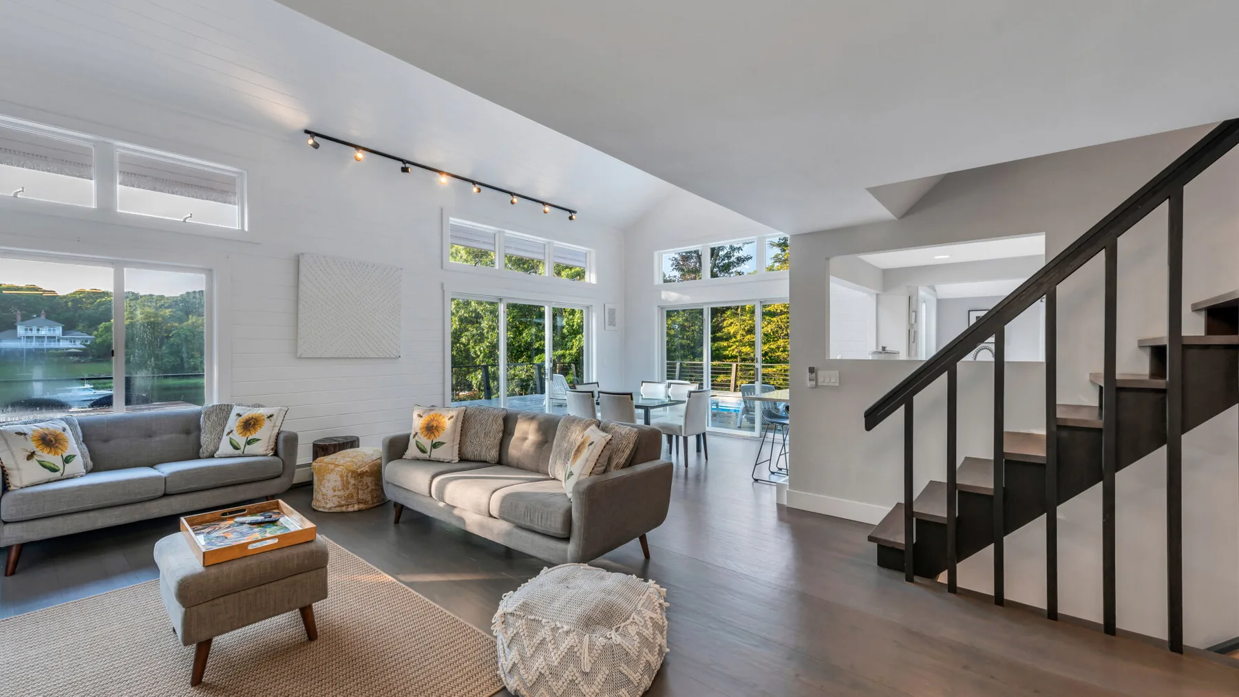 A bright living room with seating, large windows, and a staircase.