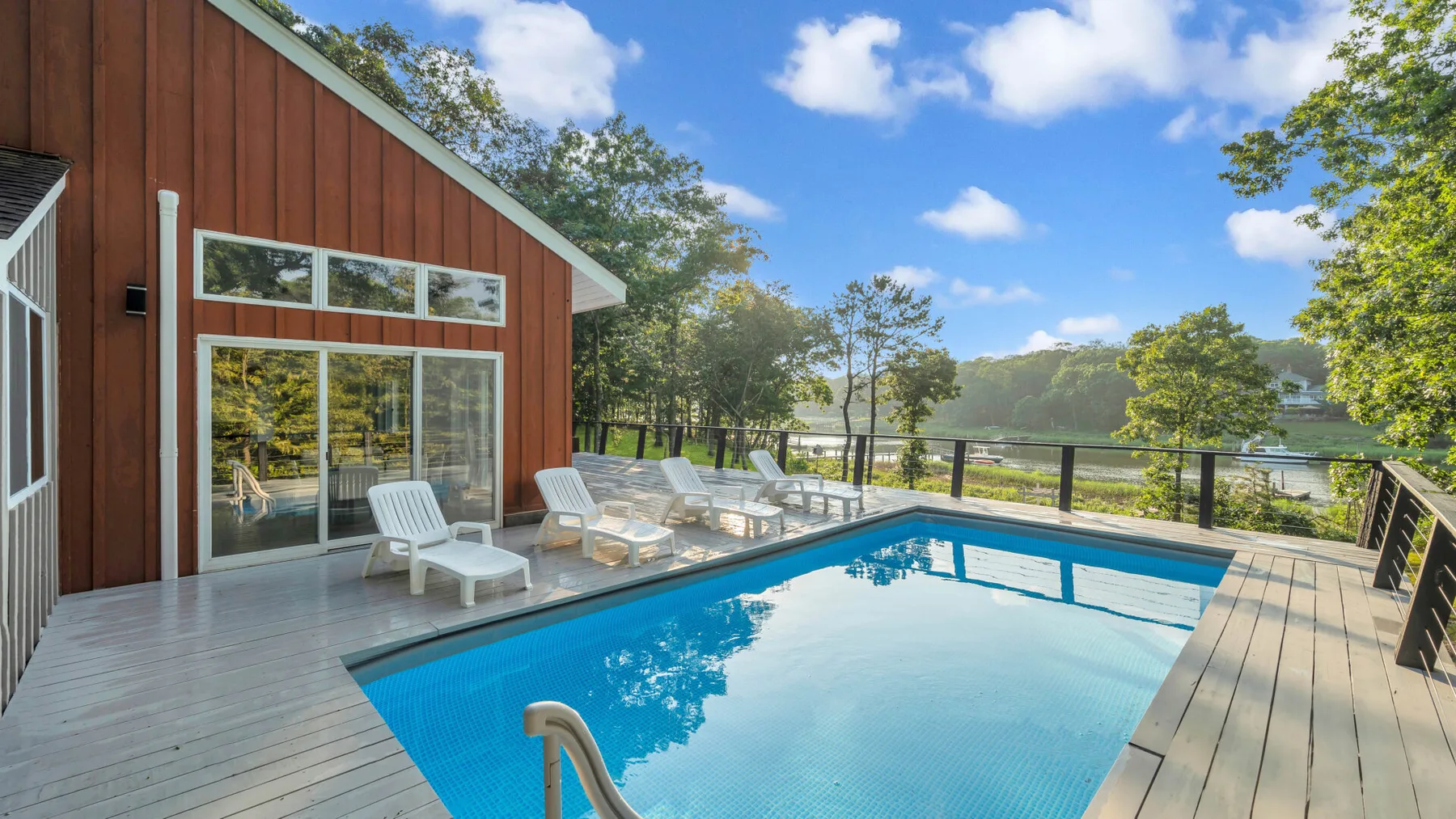 An outdoor swimming pool sits beside a wooden deck and a building.