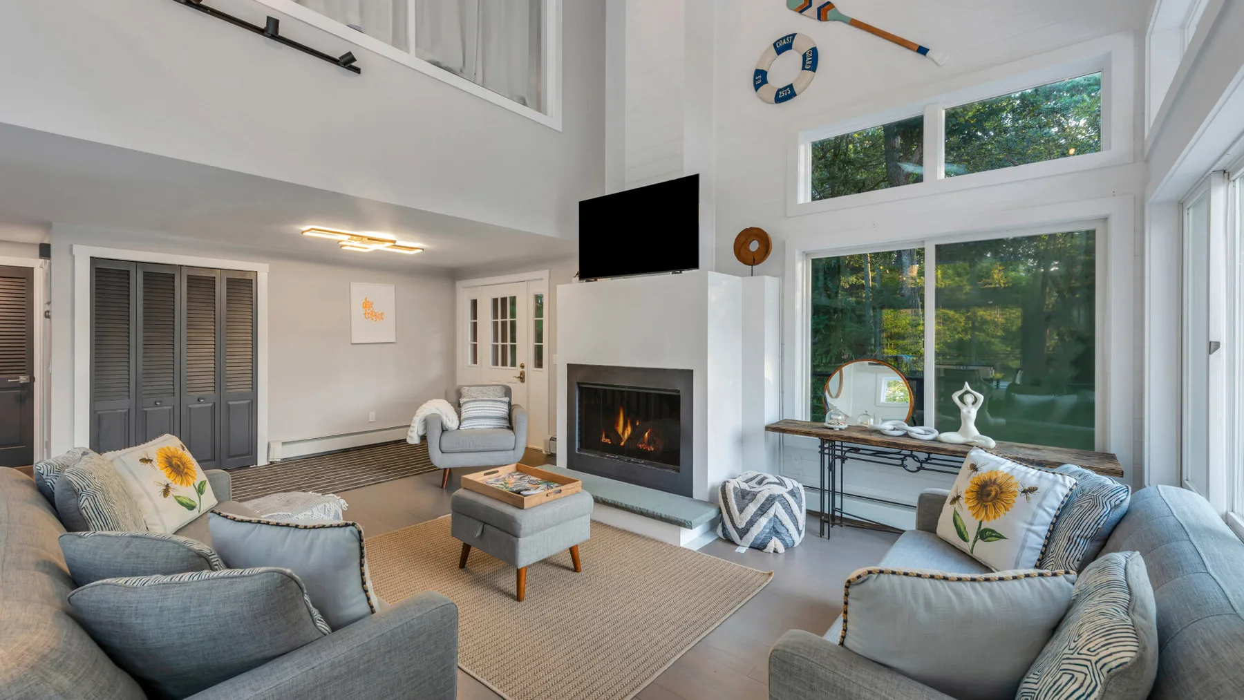 A bright living room with seating around a fireplace and large windows.
